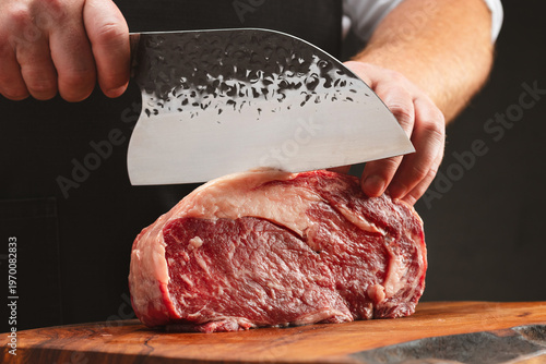 Professional butcher, chef cuts raw beef steak with sharp knife on a wooden board and wooden table. Selective focus