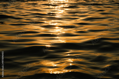 Photography Abstract view of golden sunlight reflecting on dark sea ripples during sunset, creating a luxurious and calm atmosphere