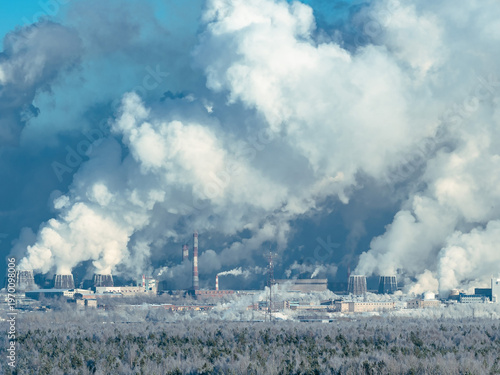 Air pollution from industrial factory chimneys and cooling towers in winter forest. Greenhouse gas causing climate change and global warming.