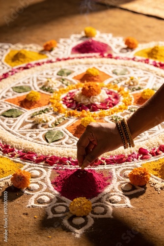 Wallpaper Mural Close-up of a person's hand creating a colorful floral rangoli design on the ground with intricate patterns and vibrant flowers. Torontodigital.ca