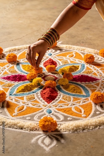 Wallpaper Mural Close-up of a woman's hand creating a colorful rangoli design on the floor with flower petals and powder in a traditional Indian setting. Torontodigital.ca