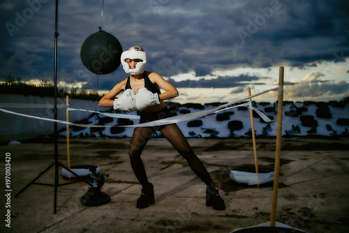 Young athletic woman wearing white boxing gloves and protective helmet moves inside a conceptual outdoor ring.