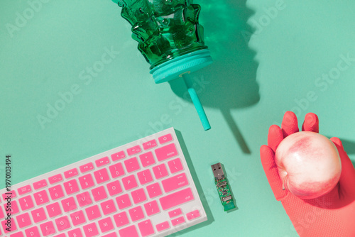 Hand in pink latex glove holding pink apple, USB board, keyboard and cup on mint background, healthy work concept, copy space