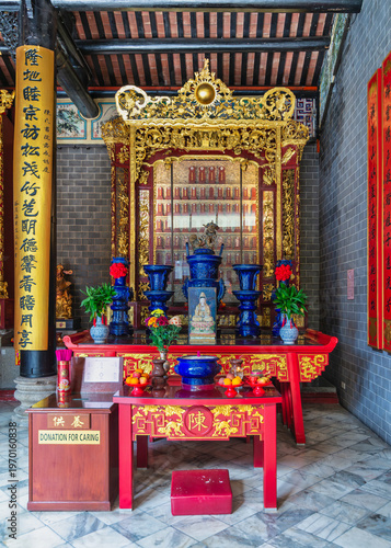 Vibrant altar with offerings, deity statue, and traditional Chinese architecture inside Chan She Shu Yuen Ancestral Hall, Kuala Lumpur Malaysia. Golden carvings, blue vases, and red accents