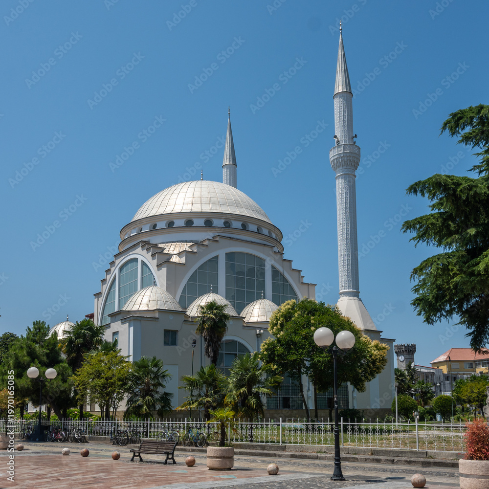 Obraz premium The modern Ebu Beker Mosque stands prominently with its striking silver dome and tall twin minarets against a brilliant blue sky in Shkoder, Albania.