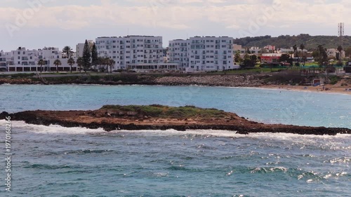 Aerial drone view of a small rocky islet surrounded by waves off the coast of Protaras, Fig Tree beach, Cyprus