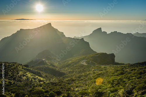 Tenerife Mountain Range With Curvy Road, Sunset Sunbeams, Misty Silhouettes and Lush Green Slopes, Dramatic Scenic Nature Panorama of Rugged Hills and Valleys