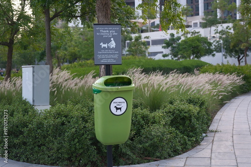 Φωτογραφία Side right angle view of green dog waste bin with sign beside manicured urban pa
