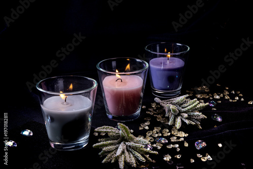 Lit scented candles in glass holders with decorative crystals and flowers on dark background spa relaxation concept