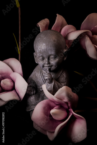 Zen monk statue with finger on lips surrounded by flowers silence and mindfulness concept