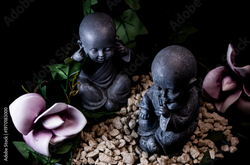 Zen monk statues in miniature garden with stones and flowers meditation and mindfulness concept
