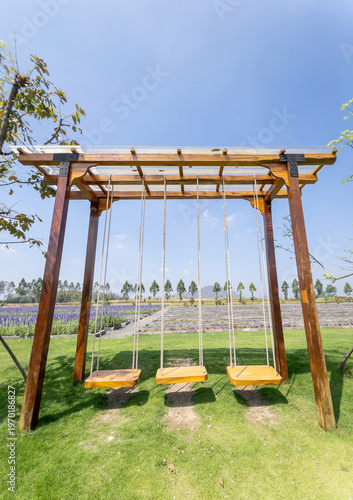 Large wooden swing on green lawn in beautiful flower garden under blue sky.