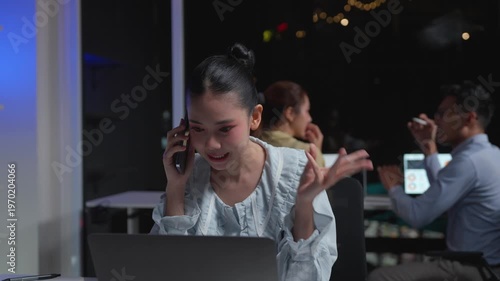 Young Asian businesswoman talking on the phone while working overtime in a modern office at night