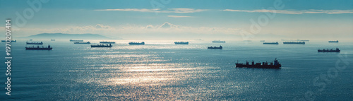 Cargo ship supply chain disruption at sea with many container vessels waiting under cloudy sky and distant island horizon