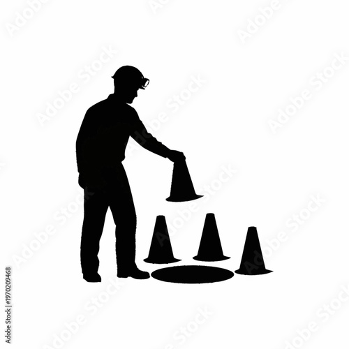 Silhouette of a construction worker placing traffic cones around a manhole.