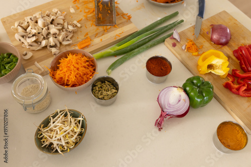 Kitchen countertop displaying assorted vegetables, spice bowls, cutting boards and chef knife