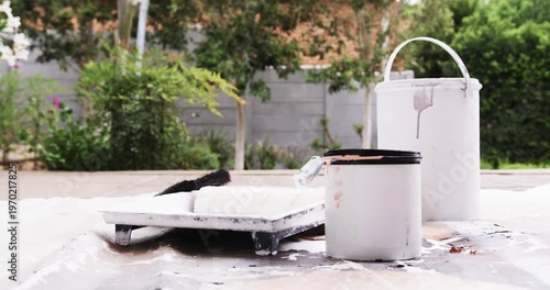 Small dark bird landing on paint roller, perching, preening on tray near paint cans in backyard