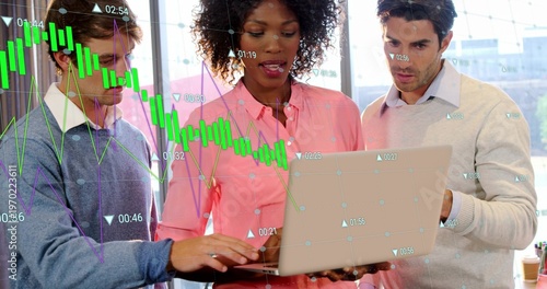 Reviewing team studying faint market overlay on silver laptop by big windows, coffee, in casual