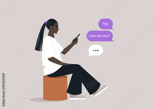 A young individual is sitting comfortably on a pouf, deeply engaged in a smartphone conversation, The casual setting invites a sense of calm and connection with friends.