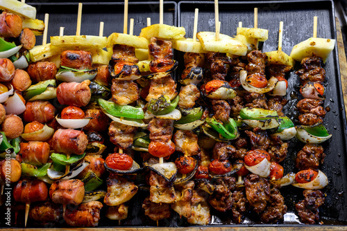 delicious grilled bbq skewers with pork chicken bacon sausage and vegetables on a black tray at a street food market