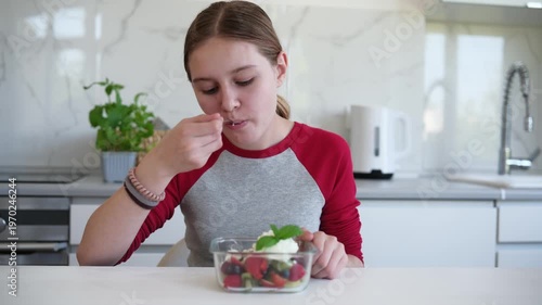 Little girl eating fruit salad with cream in kitchen in the morning