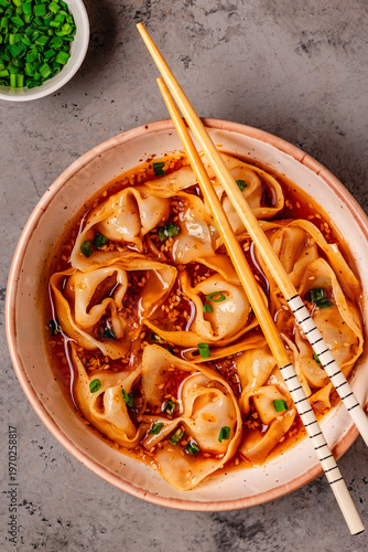 Wontons are placed in a bowl with spicy sauce.