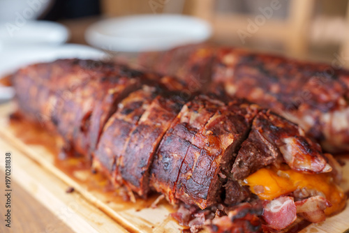 Golden-brown, crispy pork loin rests on a wooden board. Slices reveal tender meat and melted cheese inside. Juicy, smoky exterior suggests perfect grilling or roasting. Ideal for food blogs, cookbooks