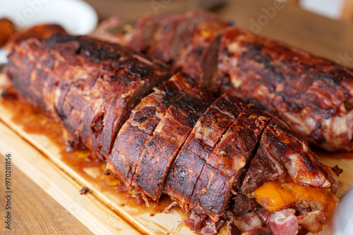 Golden-brown, crispy pork loin rests on a wooden board. Slices reveal tender meat and melted cheese inside. Juicy, smoky exterior suggests perfect grilling or roasting. Ideal for food blogs, cookbooks