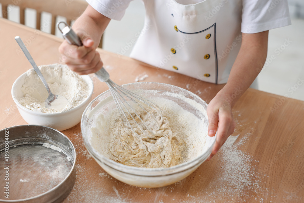 Fototapeta premium Child mixing dough in bowl at wooden table indoors, closeup