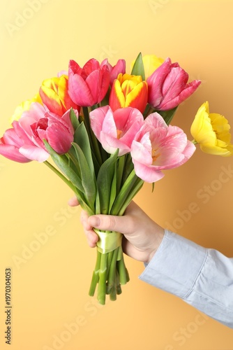 Woman with bouquet of aromatic bright tulips on yellow background, closeup. Beautiful greeting card