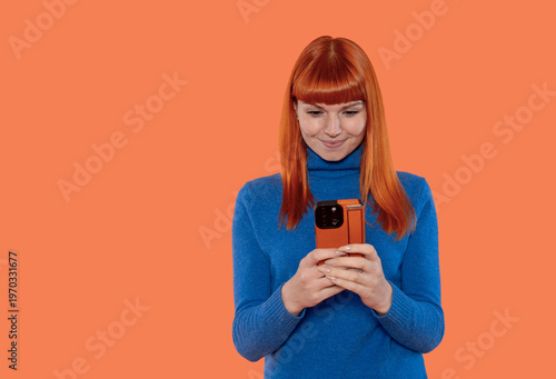 Woman uses smartphone while smiling in front of an orange background