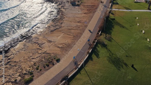 Aerial drone view of cyclists riding along coastal path in Ayia Napa, Cyprus at sunset