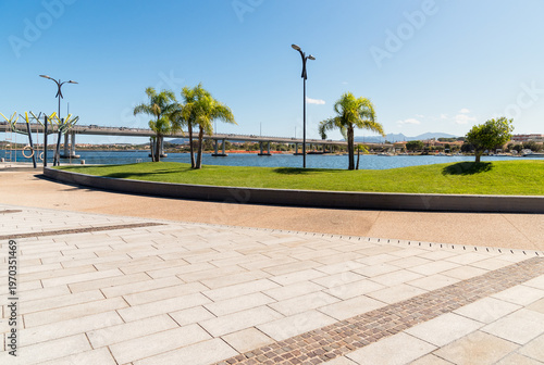 Olbia seafront with a large paved pedestrian area and view of the viaduct crossing the gulf, Sardinia, Italy. Modern waterfront with open public space, coastal landscape, and urban infrastructure.