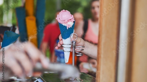 Hand holding strawberry ice cream in blue cone, refreshing sweet street food dessert