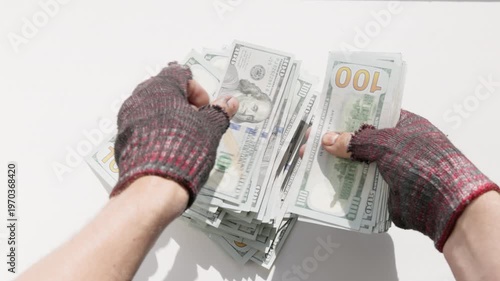 Adult beggar counts one hundred dollar bills indoors against a plain white background.