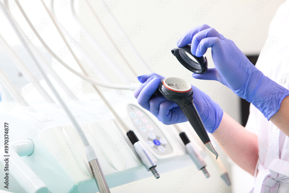Fototapeta premium Sandblasting teeth cleaning. Female dentist's hand in blue gloves holding sandblasting tool. Сoncept of dentistry and dental care. Oral hygiene. Prevention of dental diseases.