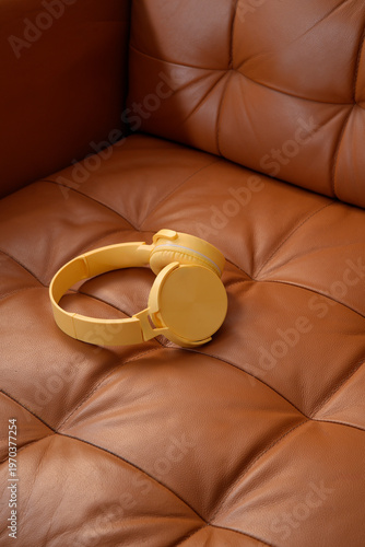 Bild auf Leinwand Yellow headphones resting on brown leather sofa
