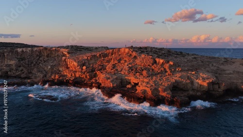 Aerial drone view of rugged coastal cliffs in Cape Greco, Cyprus, illuminated by warm sunset light