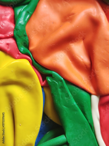 Primer plano de globos de látex desinflados con texturas rugosas y pliegues en colores naranja, amarillo, verde y rosa