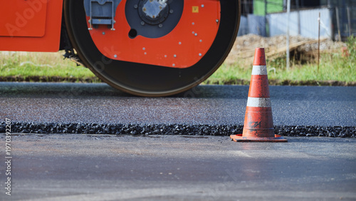 Road construction worker compacting black asphalt with heavy steamroller machine