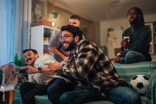 Quadro su tela Friends playing competitive video game soccer at home, enjoying beer and shared