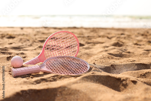 Pink beach rackets and ball resting on the sand near the ocean waves