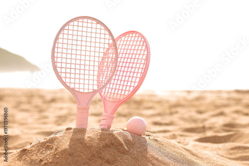 Pink beach rackets and ball resting on the sand near the ocean waves