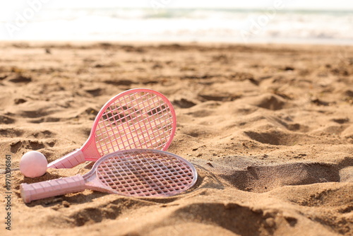 Pink beach rackets and ball resting on the sand near the ocean waves