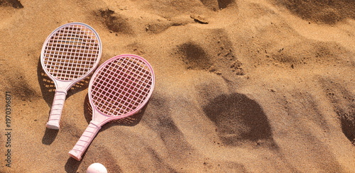 Pink beach rackets and ball resting on the sand near the ocean waves