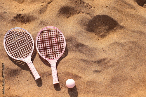 Pink beach rackets and ball resting on the sand near the ocean waves