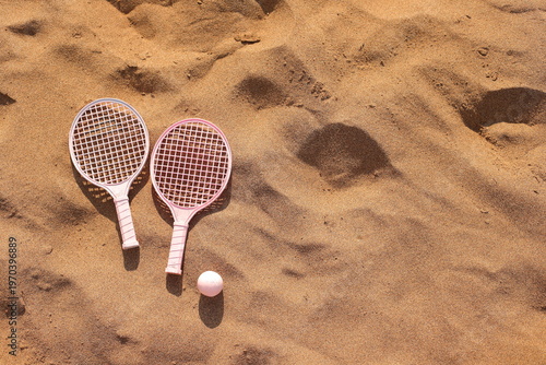Pink beach rackets and ball resting on the sand near the ocean waves