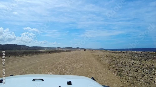 Beautiful view of Arikok National Park with dusty road seen from moving vehicle along Caribbean Sea. Aruba.