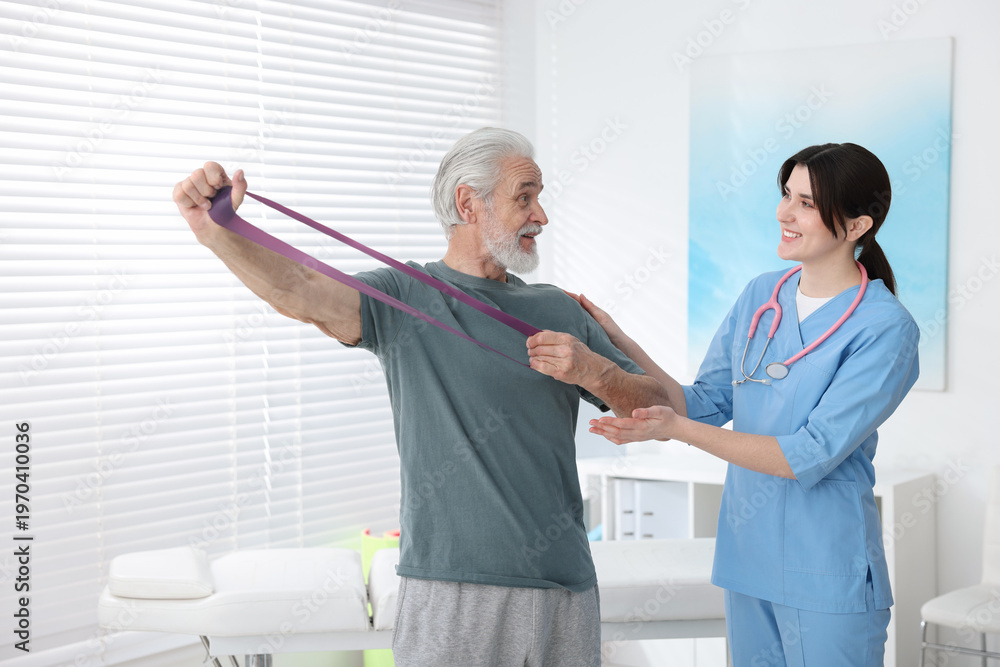 Fototapeta premium Senior man training with resistance band under physiotherapist supervision indoors