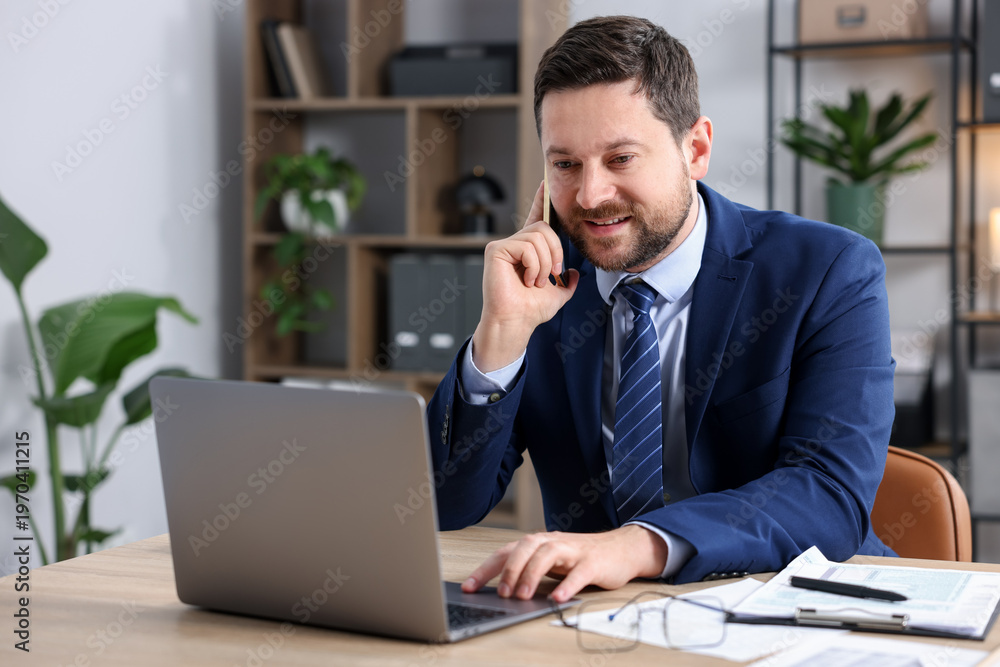 Obraz premium Man talking on smartphone at wooden desk indoors